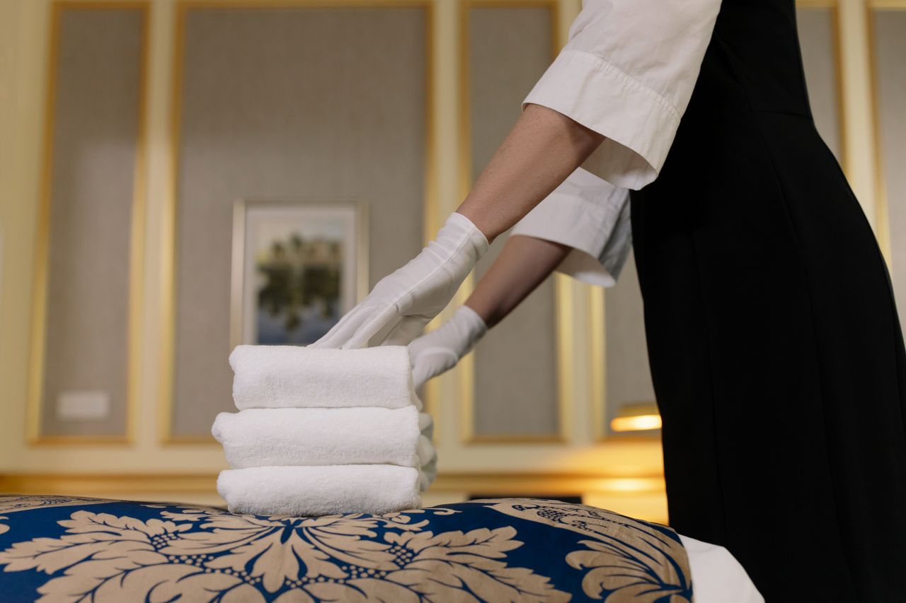 hero-img A hotel housekeeper neatly stacks fresh towels in a luxurious room setting.